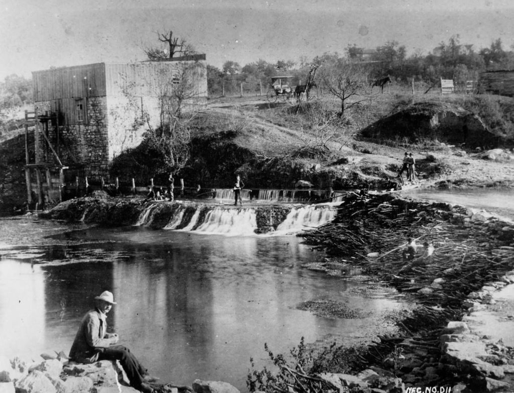 Black and white photo of Barton springs with a man sitting on a rock in the front around the spring