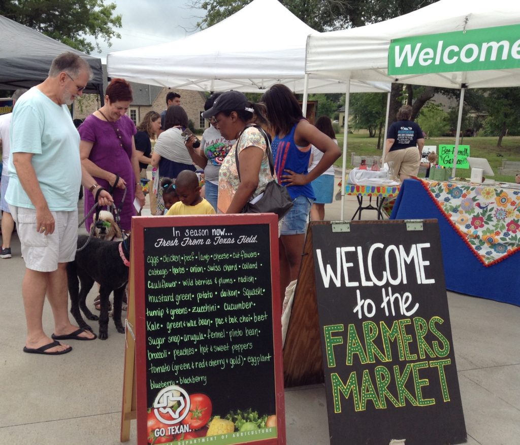 Group of individuals standing behind signs for the Farmer Market