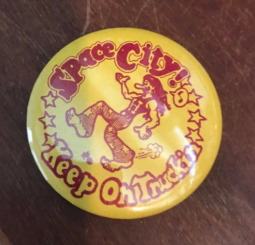 Yellow Button with Space City on it and a figure in red
